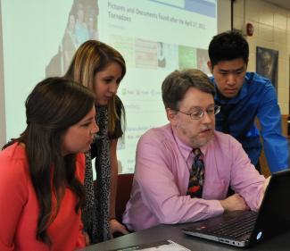 Dr. John Knox looks at a laptop with students 