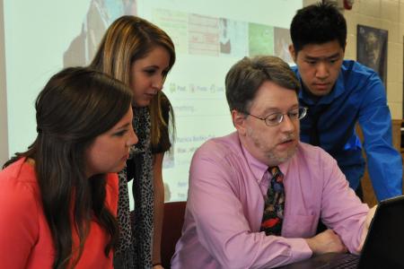 Dr. John Knox looks at a laptop with students 